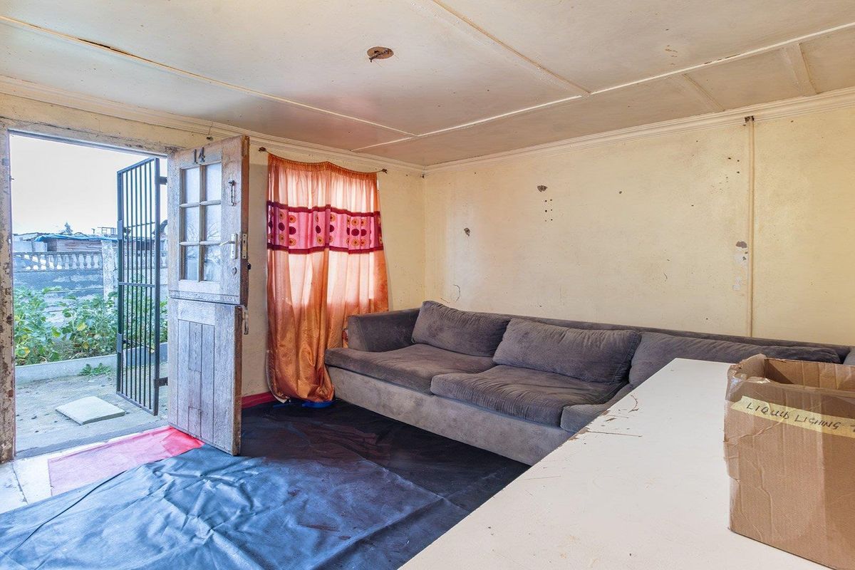 A living room area featuring a timber entrance door with security gate, requiring significant cosmetic updates and wall repairs.