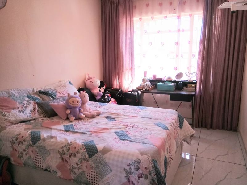 A bedroom featuring tiled flooring and a large window with curtains, providing natural light to the space.