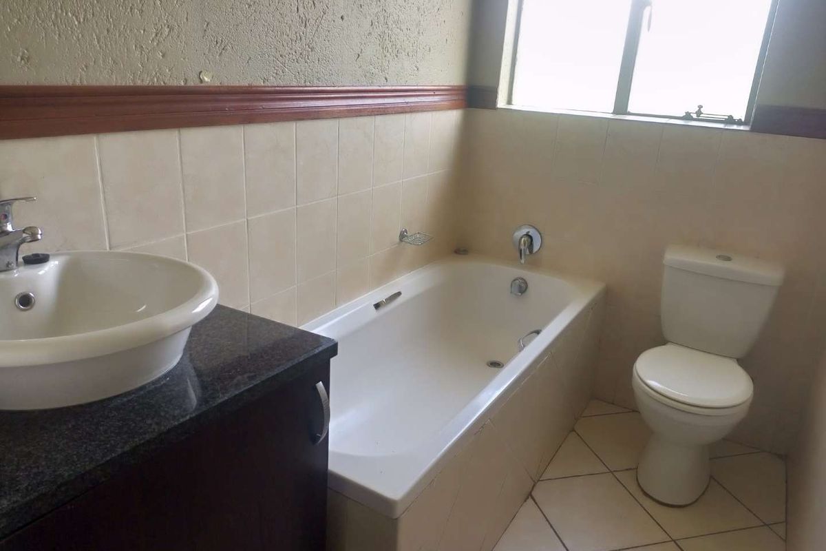 A functional bathroom featuring a built-in vanity with granite countertop, a standard bathtub, and a toilet, finished with neutral wall and floor tiles.