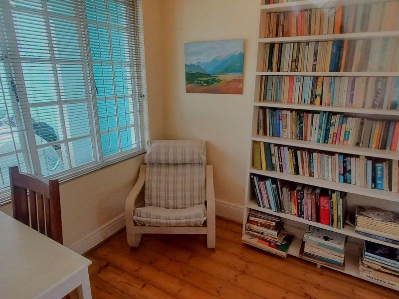 A cozy living area featuring warm timber flooring, a large built-in bookshelf, and natural light filtered through venetian blinds.