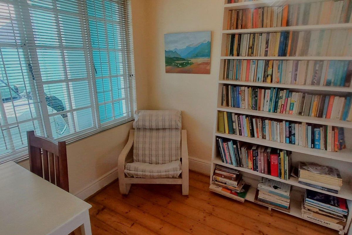 A cozy living area featuring warm timber flooring, a large built-in bookshelf, and natural light filtered through venetian blinds.