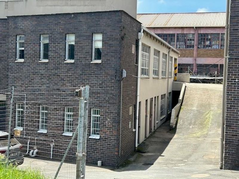 Rear exterior view of an industrial building featuring brick facade, security-barred windows, and a concrete access ramp.