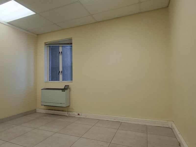 A vacant office space featuring tiled flooring, a suspended ceiling, and a wall-mounted HVAC unit, providing a clean and functional workspace.