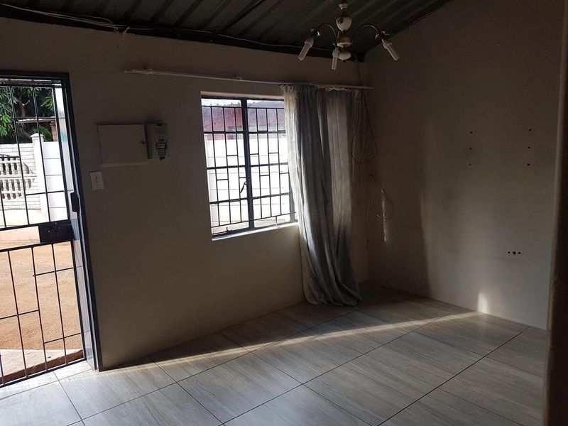 An empty living room featuring tiled flooring, security gate access, and burglar bars on the window, requiring minor cosmetic updates.