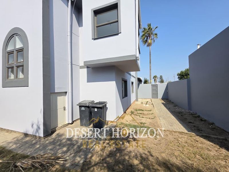 Rear view of the property featuring a paved walkway, boundary wall, and modern exterior finishes with side access.