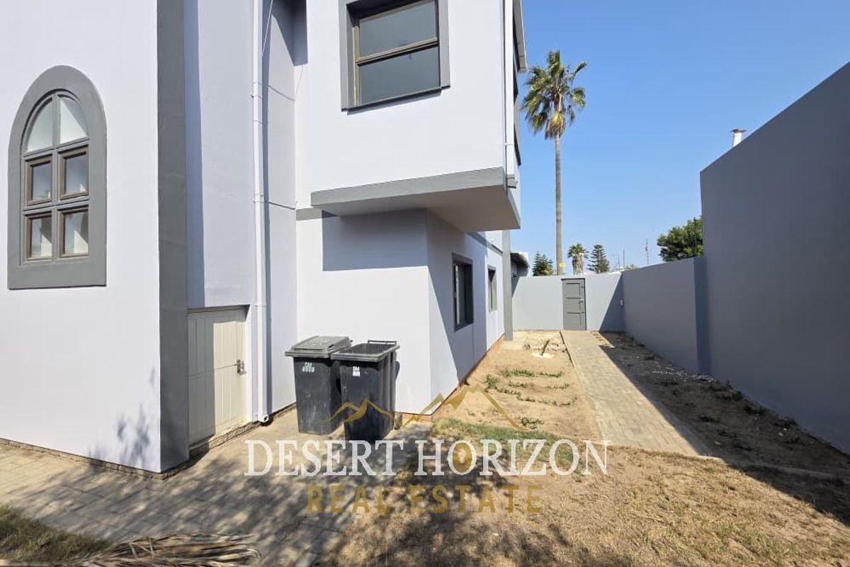 Rear view of the property featuring a paved walkway, boundary wall, and modern exterior finishes with side access.