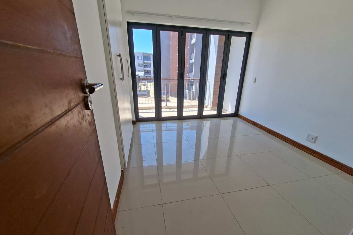 A bright, empty bedroom featuring polished tile flooring, built-in cupboards, and large glass folding doors that open onto a private balcony.