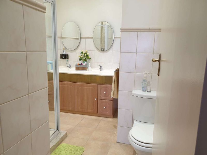 A functional bathroom featuring a double vanity with built-in cabinetry, a shower enclosure, and a standard toilet with neutral wall and floor tiling.