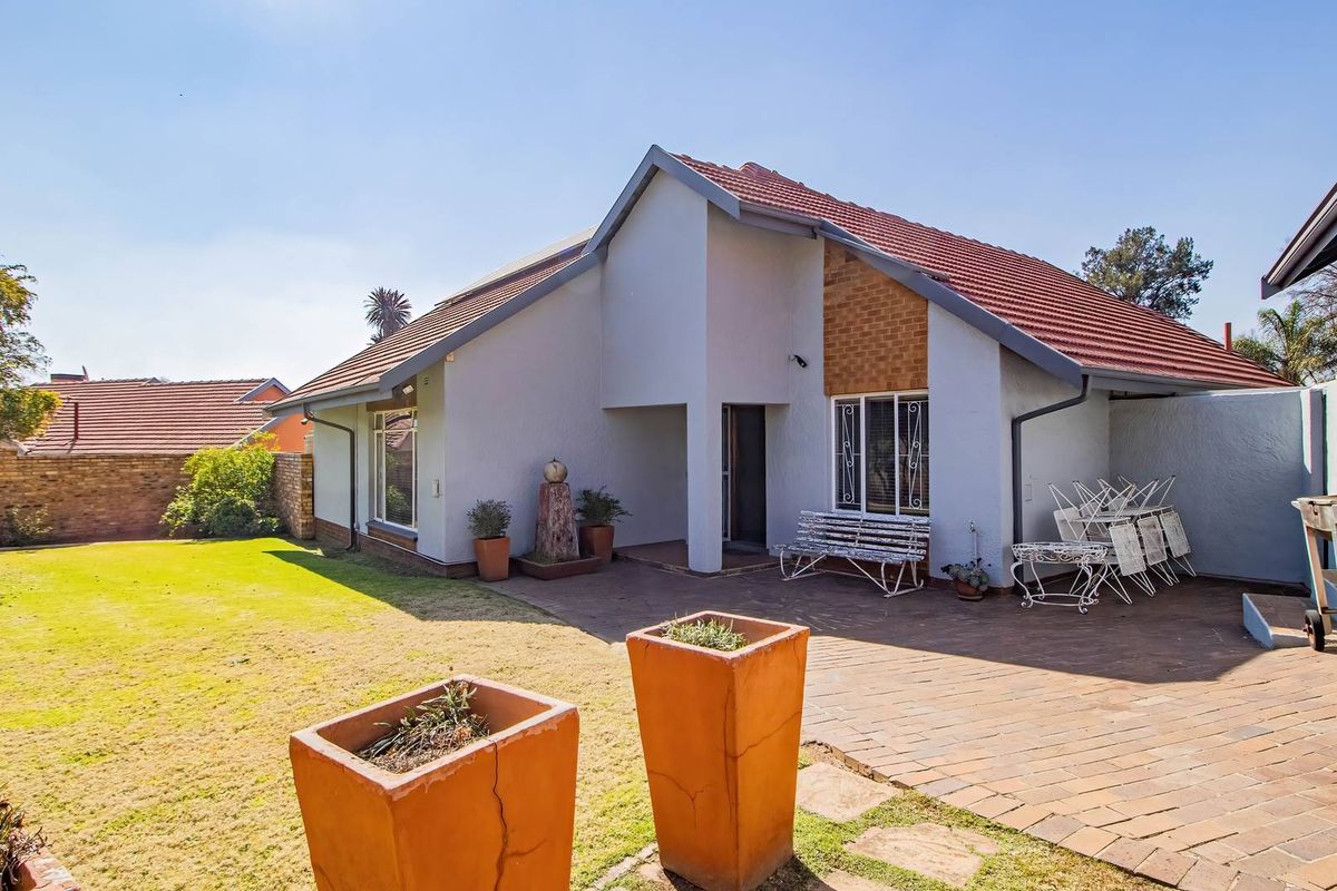 Rear view of the house featuring a paved patio area, tiled roof, and a well-maintained garden space.