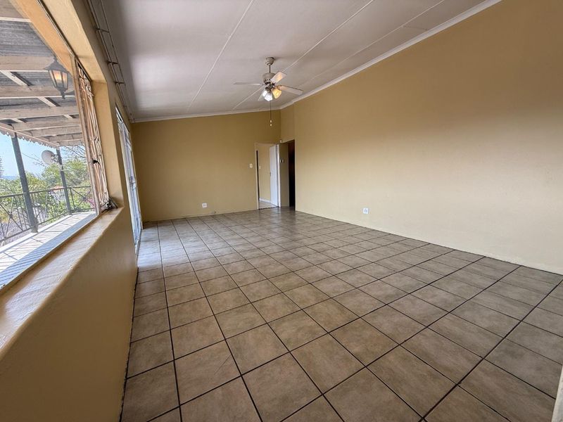 Spacious, empty living area featuring neutral tiled flooring, a ceiling fan, and direct access to an outdoor balcony through sliding glass doors.