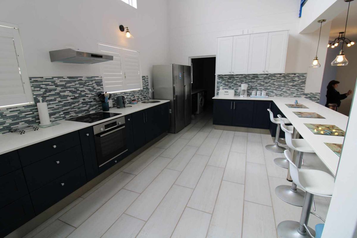 Modern kitchen featuring dark cabinetry, white countertops, a mosaic tile backsplash, built-in oven, extractor fan, and a breakfast bar with pendant lighting.