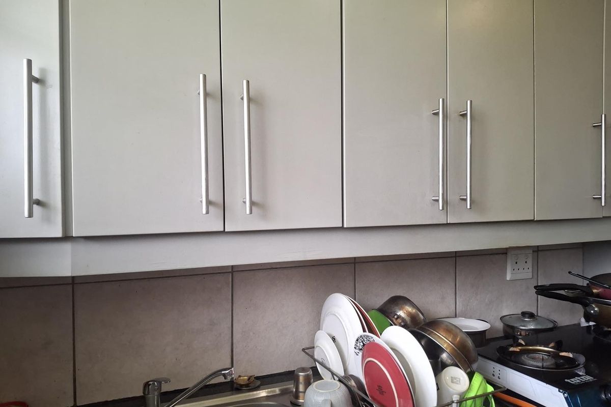 A functional kitchen area featuring neutral-toned built-in cabinetry, a stainless steel sink with mixer tap, and a tiled backsplash.