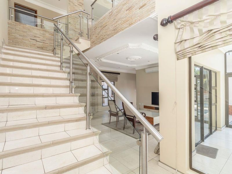 Spacious entrance hall featuring a tiled staircase with a modern glass balustrade, stone feature wall, and decorative ceiling molding leading into the living area.