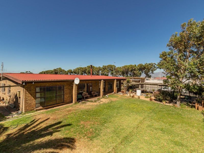 Rear view of a single-story brick house featuring a red corrugated metal roof, a covered patio area, and a spacious backyard with established lawn.