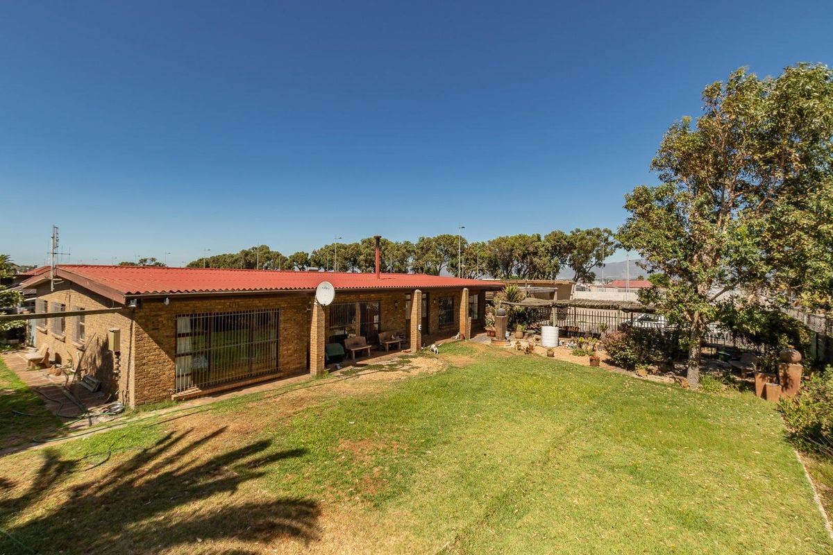 Rear view of a single-story brick house featuring a red corrugated metal roof, a covered patio area, and a spacious backyard with established lawn.