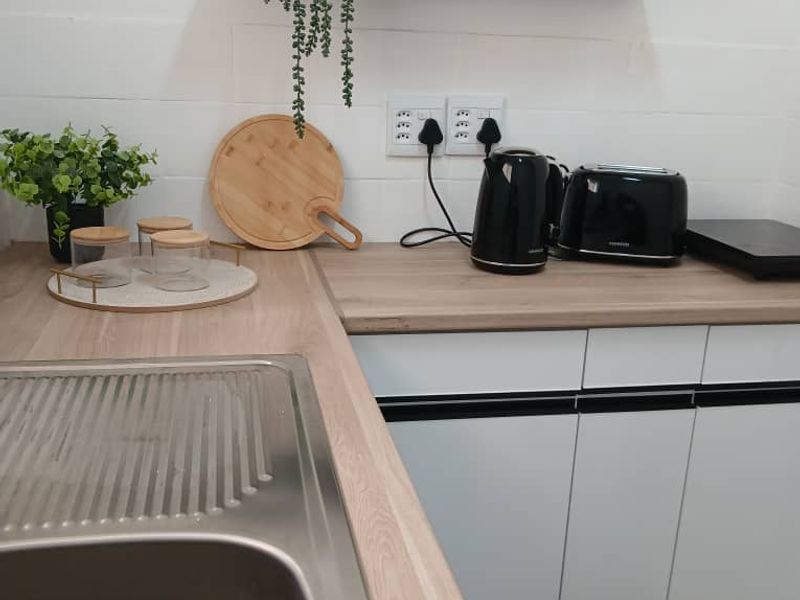 A modern kitchen area featuring white cabinetry, a wood-look laminate countertop, a stainless steel sink, and a floating shelf with a tiled backsplash.