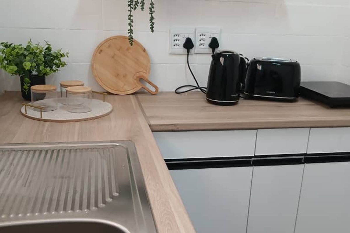 A modern kitchen area featuring white cabinetry, a wood-look laminate countertop, a stainless steel sink, and a floating shelf with a tiled backsplash.