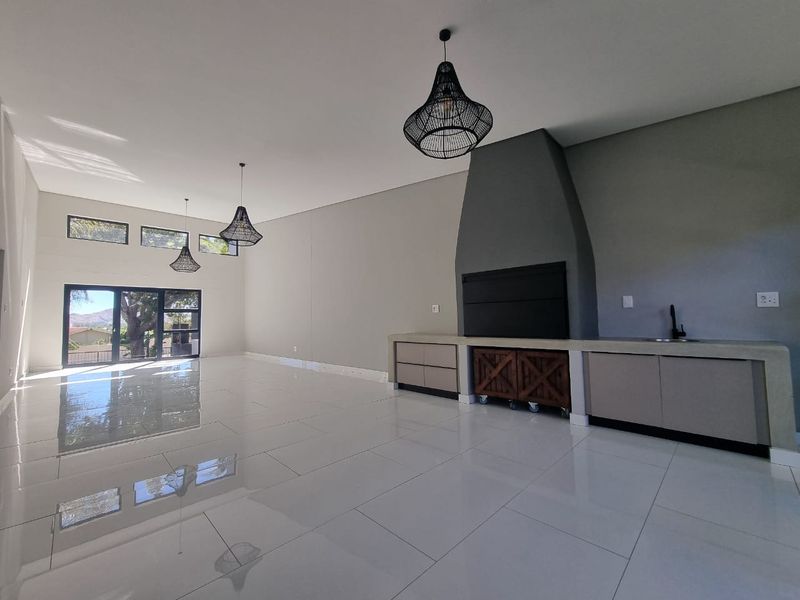 Spacious open-plan living area featuring high ceilings, polished tile flooring, a modern built-in fireplace, and integrated cabinetry with a sink.