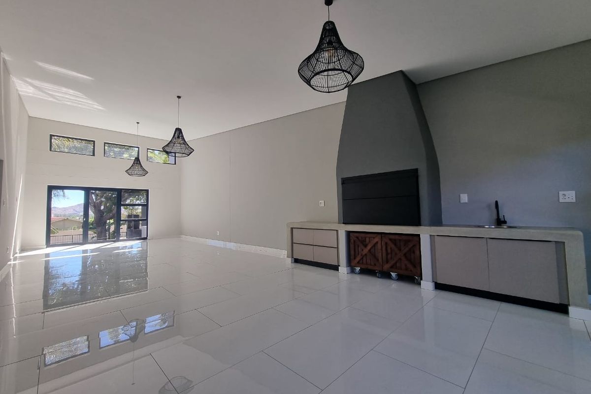 Spacious open-plan living area featuring high ceilings, polished tile flooring, a modern built-in fireplace, and integrated cabinetry with a sink.