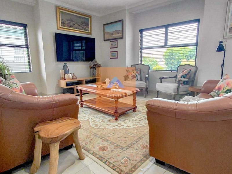 A comfortable living room featuring tiled flooring, large windows with venetian blinds, and a neutral color palette.