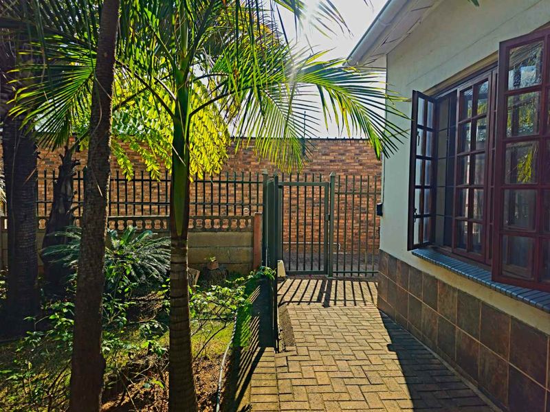 A side garden pathway featuring brick paving, a secure metal gate, and a brick boundary wall alongside the exterior of the house.
