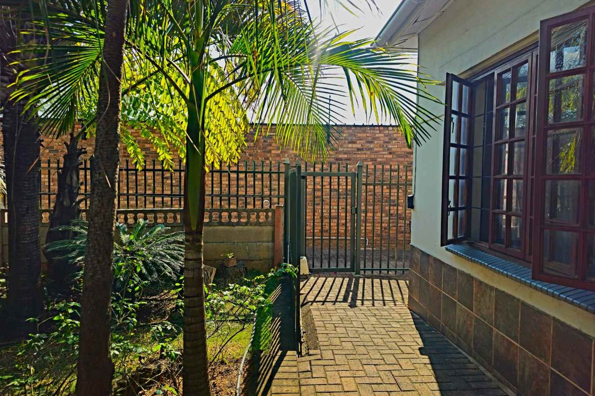 A side garden pathway featuring brick paving, a secure metal gate, and a brick boundary wall alongside the exterior of the house.