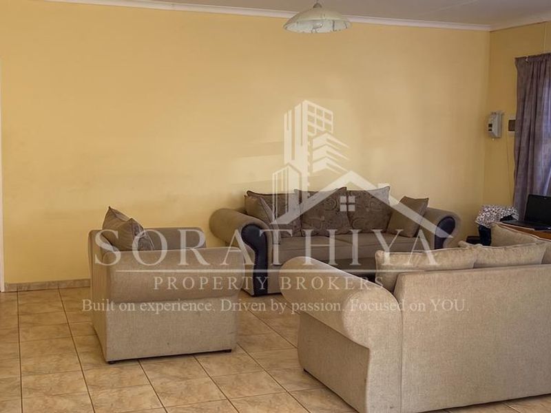 A spacious living room featuring neutral ceramic floor tiles and coved ceiling cornicing, providing a functional and well-lit living area.