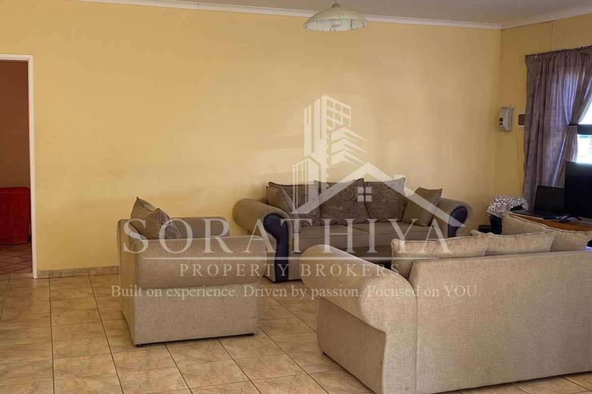 A spacious living room featuring neutral ceramic floor tiles and coved ceiling cornicing, providing a functional and well-lit living area.