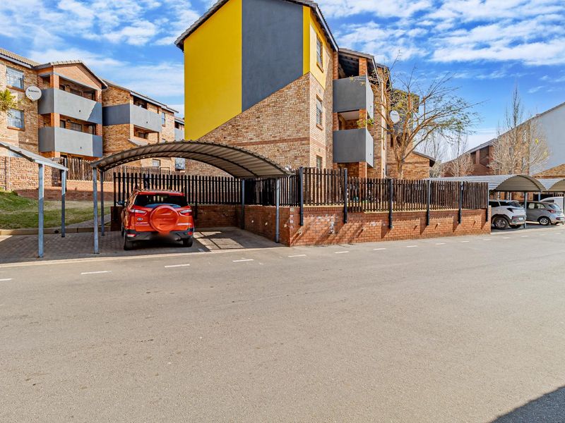 Exterior view of an apartment complex featuring brick facades, covered parking carports, and paved driveway access.