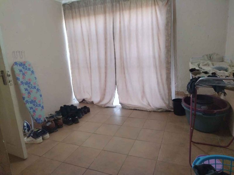 A living area featuring tiled flooring and a sliding glass door, currently showing signs of wear and wall surface damage.