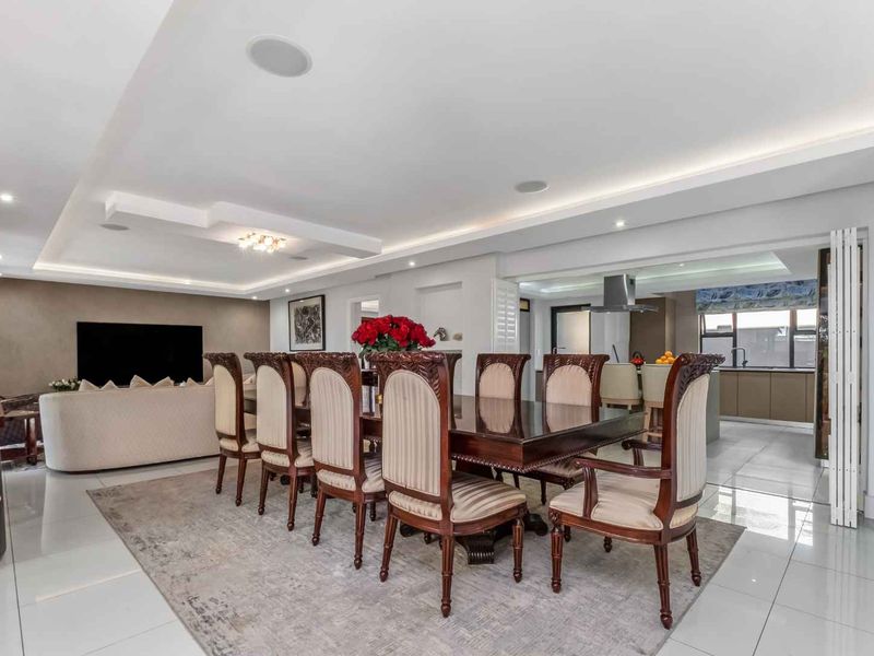 Spacious open-plan living and dining area featuring modern recessed ceiling lighting, cove lighting, and polished porcelain floor tiles, seamlessly connected to a contemporary kitchen.