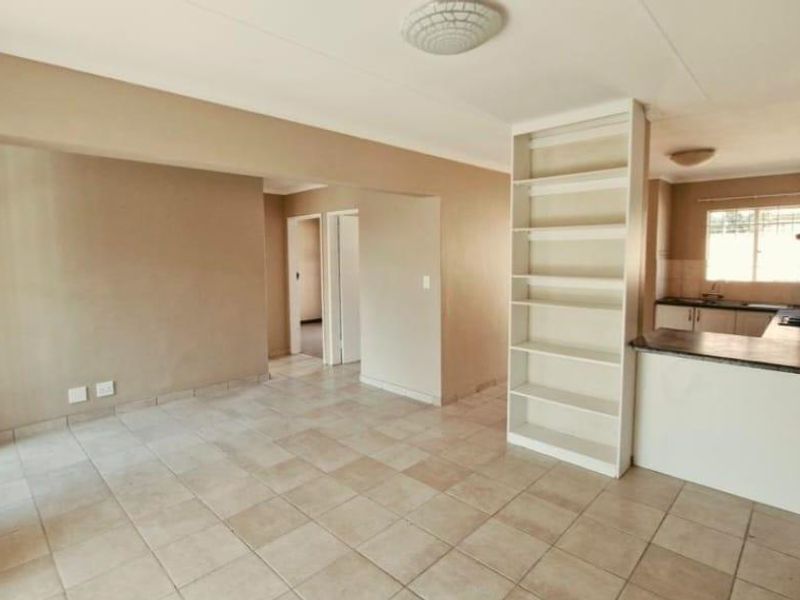 Open-plan living and kitchen area featuring tiled flooring, built-in shelving, and functional kitchen cabinetry with a countertop hob.
