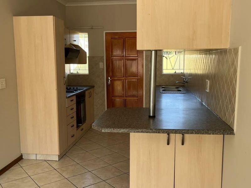A functional kitchen featuring light wood-finish cabinetry, laminate countertops, built-in oven with hob, and tiled flooring, offering a clean and practical workspace.