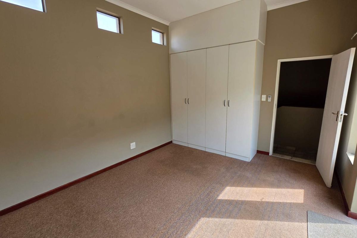 A bedroom featuring built-in cupboards, carpeted flooring, and high-level clerestory windows providing natural light.