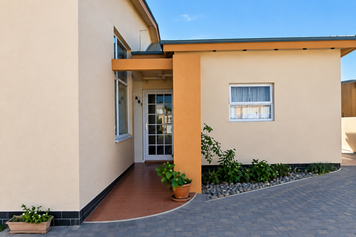 A well-maintained front entrance featuring a tiled porch, paved driveway, and clean exterior facade with modern window finishes.