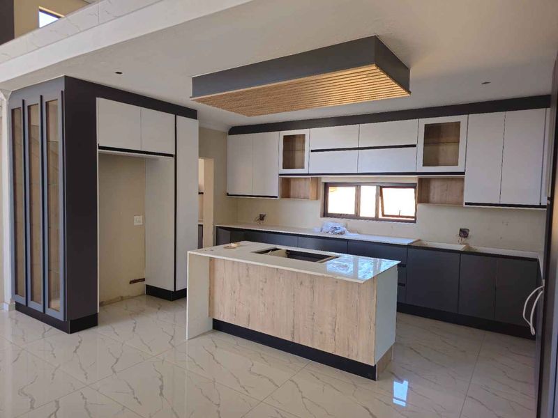 Modern, newly installed kitchen featuring a central island, sleek two-tone cabinetry, stone countertops, and a decorative suspended ceiling feature, currently awaiting final appliance installation.