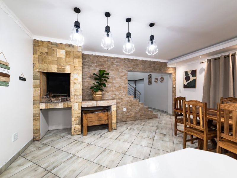 Spacious living area featuring a prominent stone-clad indoor braai, tiled flooring, and modern pendant lighting, creating a warm and inviting atmosphere.