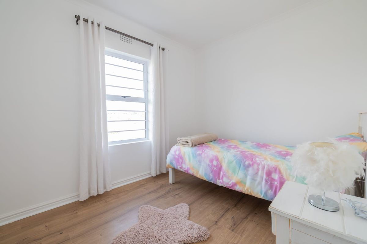 A bright and clean bedroom featuring modern laminate flooring and a functional louvre window, providing a neutral canvas for personalization.