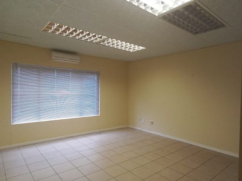A vacant office space featuring tiled flooring, recessed lighting, a split-system air conditioner, and large windows with fitted venetian blinds.