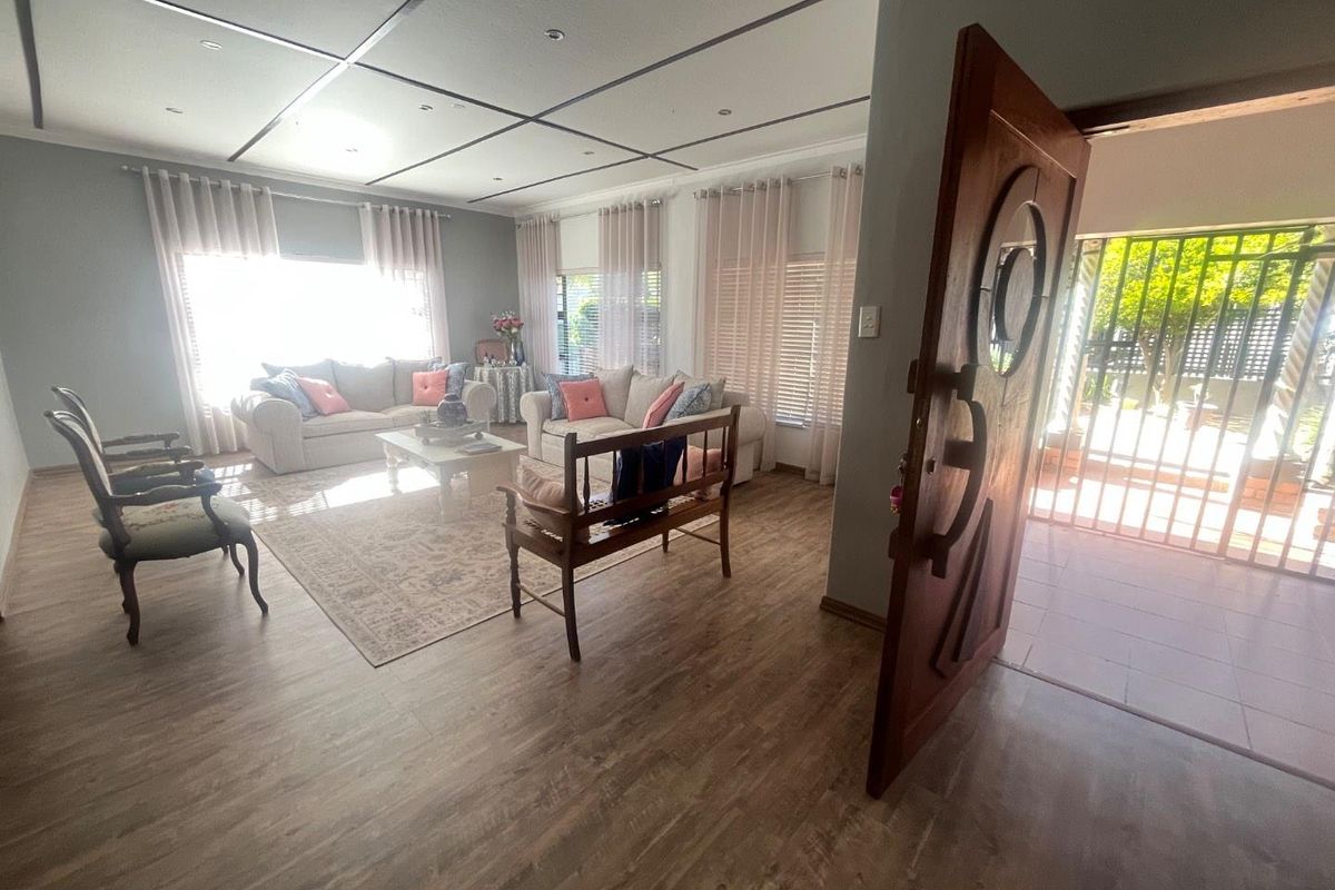 Spacious living room featuring laminate flooring, recessed ceiling lighting, and a solid timber front door with an integrated security gate.