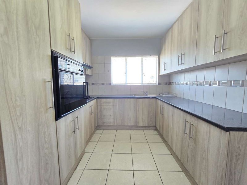A clean, functional kitchen featuring light wood-grain cabinetry, dark countertops, built-in oven, and tiled flooring with ample storage space.