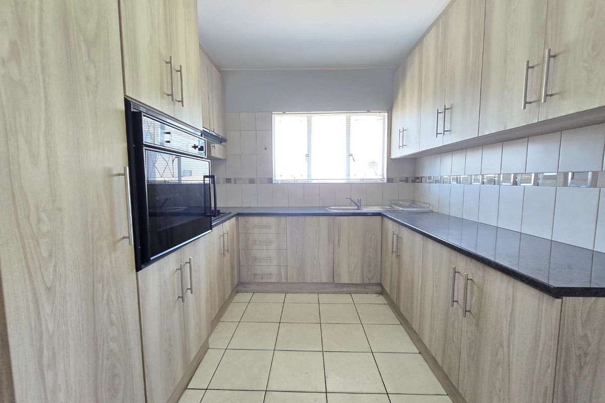 A clean, functional kitchen featuring light wood-grain cabinetry, dark countertops, built-in oven, and tiled flooring with ample storage space.