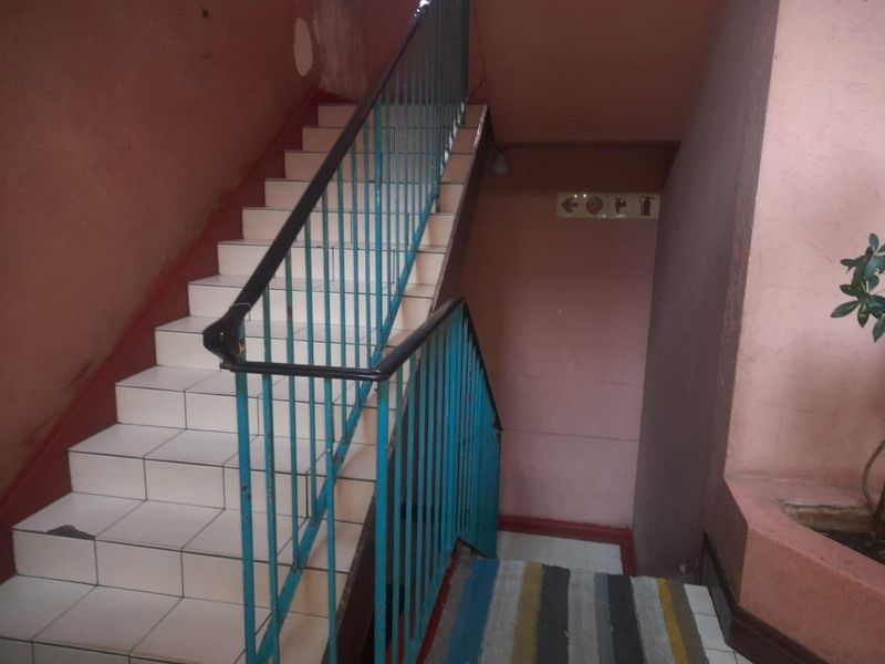 A communal stairwell featuring tiled steps and a metal balustrade, showing signs of wear and requiring cosmetic maintenance.