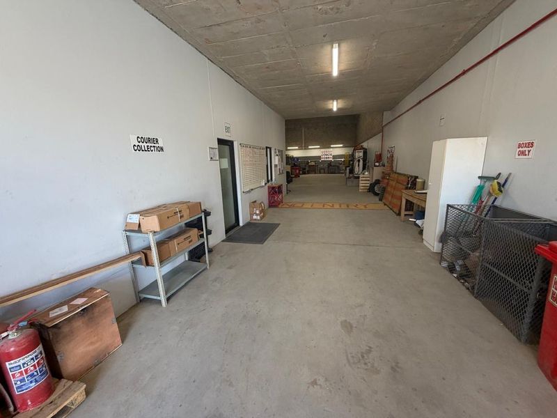 A functional utility or storage corridor featuring exposed concrete ceilings, industrial lighting, and concrete flooring, currently utilized for courier and storage operations.