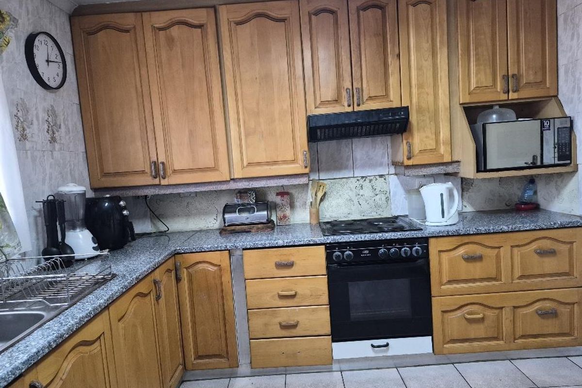 A functional kitchen featuring traditional timber cabinetry, granite-look laminate countertops, a built-in oven with hob, and an integrated extractor fan.