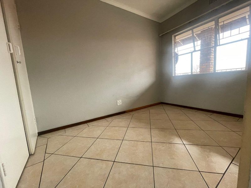 An empty bedroom featuring neutral tiled flooring, a built-in cupboard, and a window with security bars.