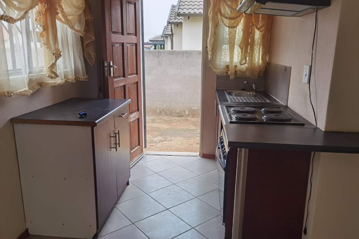 Compact kitchen featuring built-in cabinetry, an electric hob with extractor fan, and direct access to the rear exterior area.