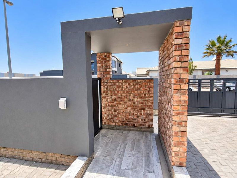 A modern front entrance featuring a brick and rendered pillar design with a paved walkway and secure gated access.