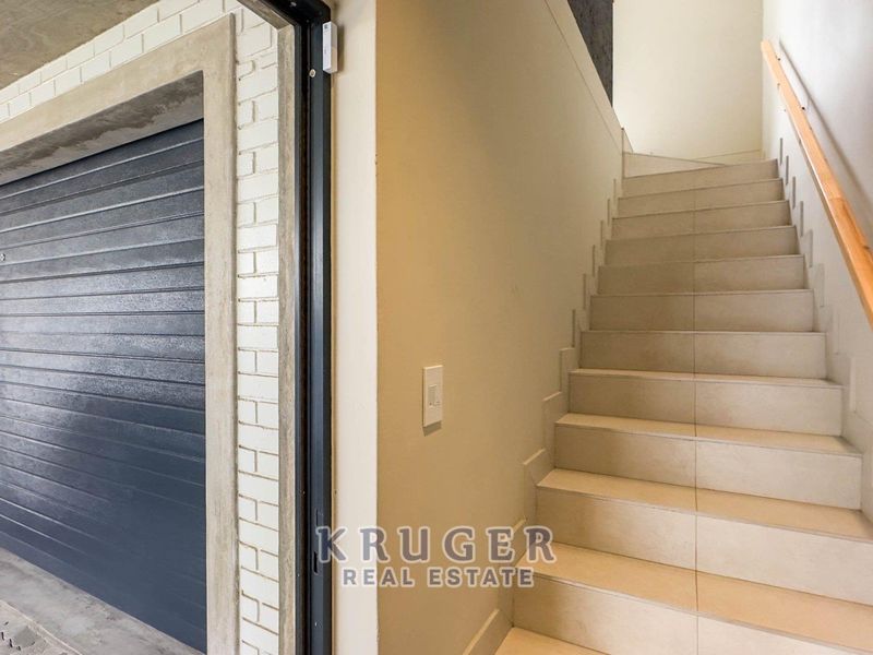 Interior view of a garage featuring a modern sectional door and a tiled staircase with a wooden handrail leading to the upper level.