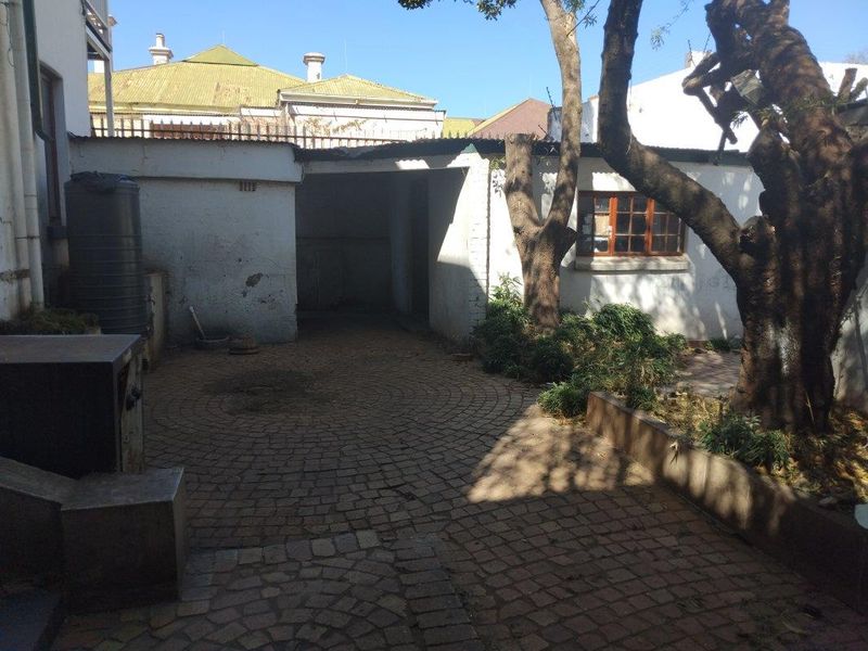 A rear courtyard area featuring paved flooring, a water tank, and mature trees, requiring maintenance to the exterior wall finishes.